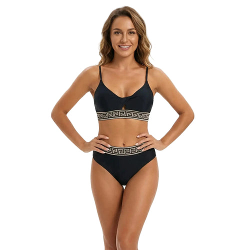 Femme portant un maillot de bain deux pièces noir avec des bordures à motifs grecs dorés sur fond blanc.