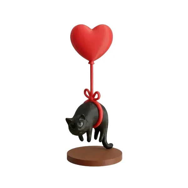 Figurine chat flottant avec ballon cœur rouge, chat noir suspendu par une corde rouge sur socle marron.