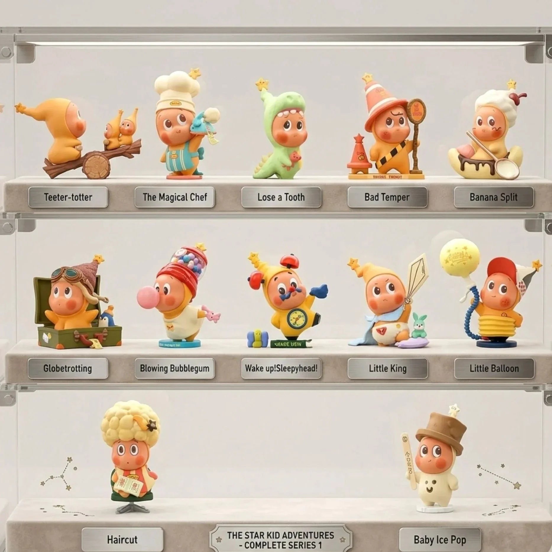 Une vitrine de collection transparente en acrylique à trois étagères contenant la collection 'The Star Kid Adventures - Complete Series 1'. Chaque étagère présente des figurines en vinyle distinctes avec des étiquettes individuelles en métal comme 'Teeter-totter', 'Globetrotting', et 'Little King'. L'étagère du milieu contient la figurine 'Little Balloon'. Les étagères sont éclairées par des lumières LED douces et intégrées. L'arrière-plan de la vitrine présente un motif de constellation subtil.